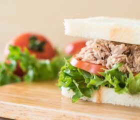 A tuna sandwich with tomato and lettuce sitting on a cutting board.