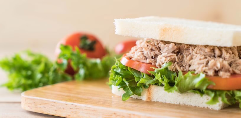 A tuna sandwich with tomato and lettuce sitting on a cutting board.