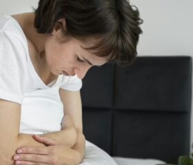 Woman sitting on her bed clutching her stomach and experiencing postpartum cramping.