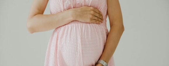 Pregnant woman in pink maternity dress holding her baby bump.