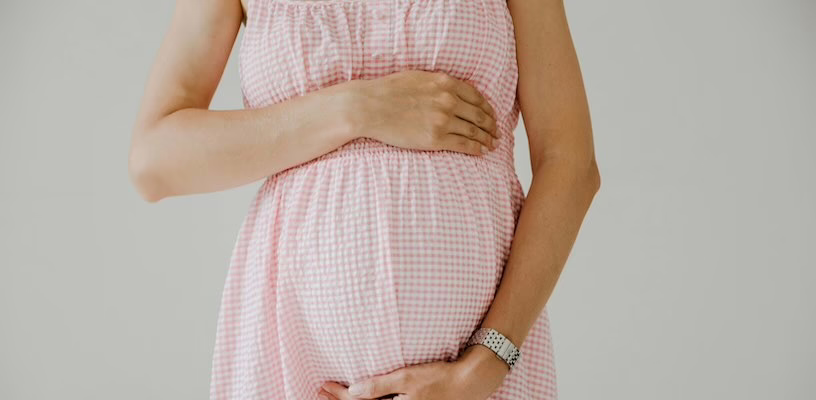 Pregnant woman in pink maternity dress holding her baby bump.
