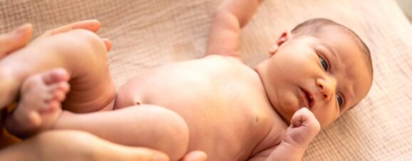 A newborn lying on a blanket with his arms extended after being startled.