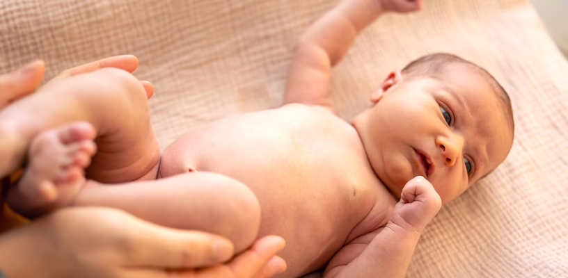 A newborn lying on a blanket with his arms extended after being startled.